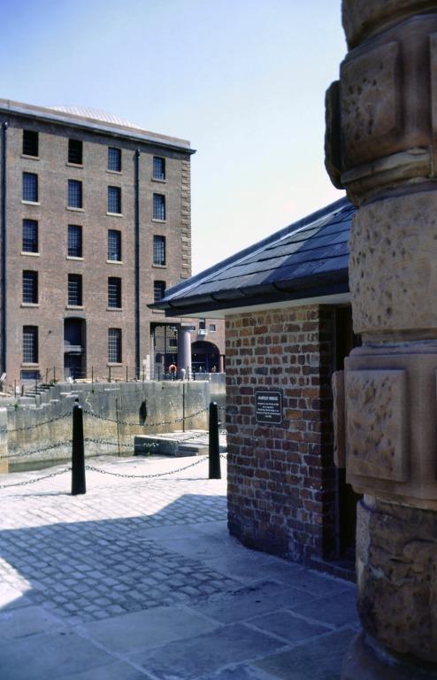 Photograph of renovation of Albert Dock, Liverpool, Block D, Merseyside Maritime Museum, near completion, section of west elevation and section of Block E, plus the Hartley swing bridge and dock gate control lodge set into a free standing section of the o card